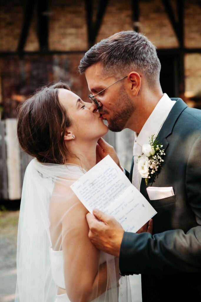 Romantischer Kuss, während der Bräutigam einen Zettel hält